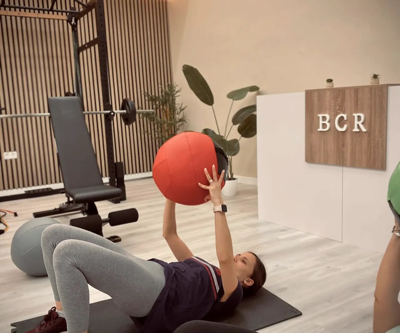 Trabajo de suelo con balón medicinal en la sala luminosa, con la recepción de BCR al fondo